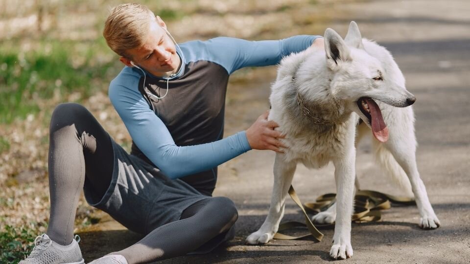 Zdjęcie przedstawia młodego mężczyznę w sportowym stroju odpoczywającego po sporcie z psem